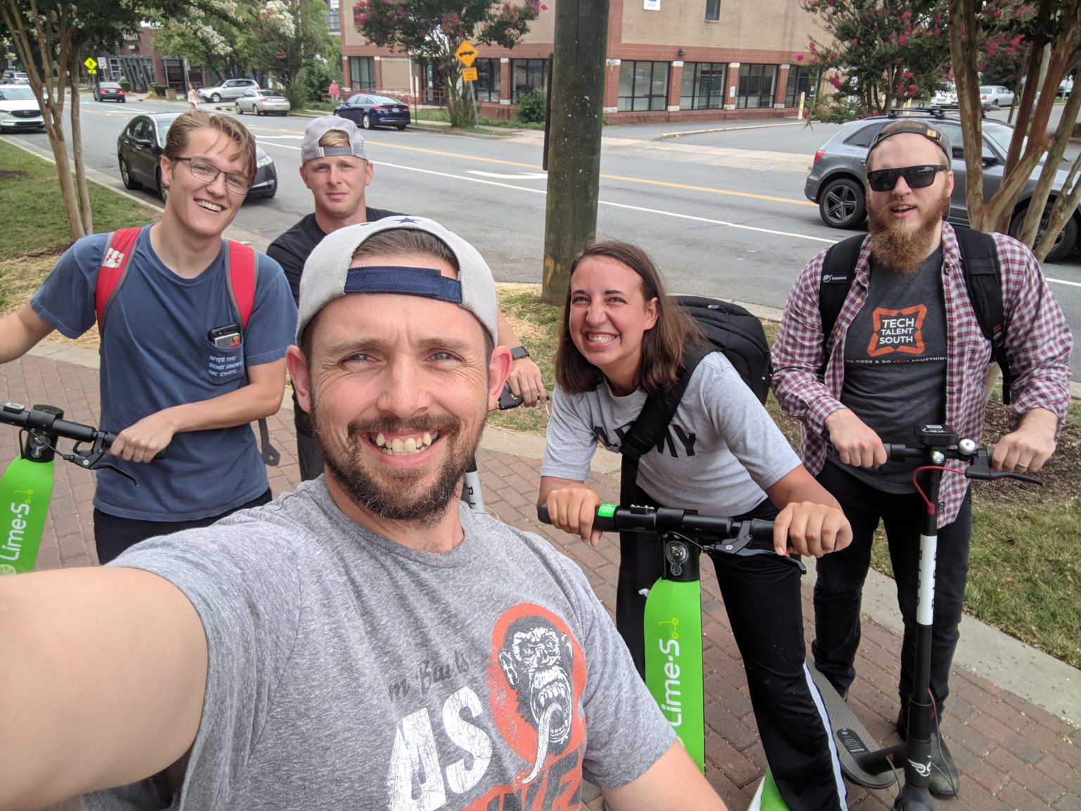 Five people posing for a selfie on scooters on a sidewalk