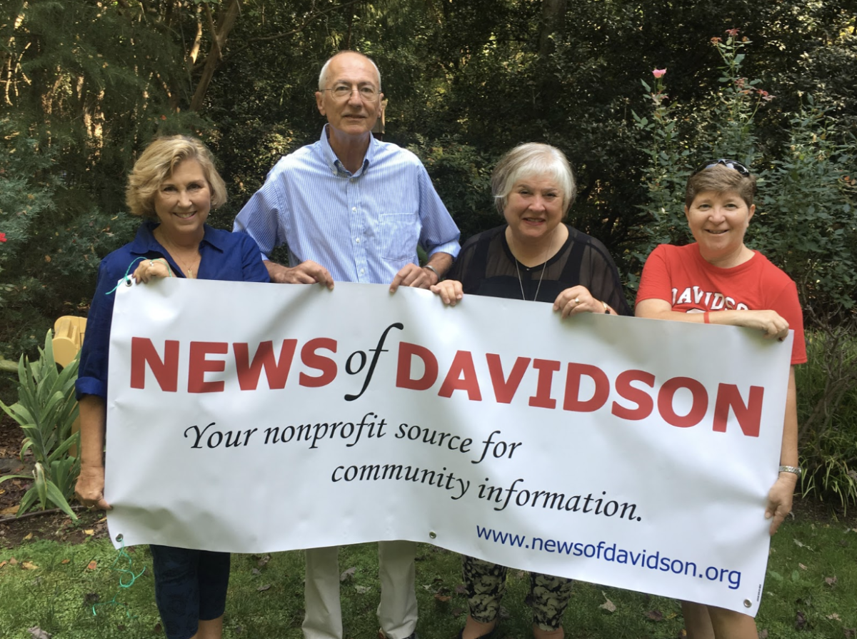 Members of the News of Davidson pose behind a News of Davidson banner