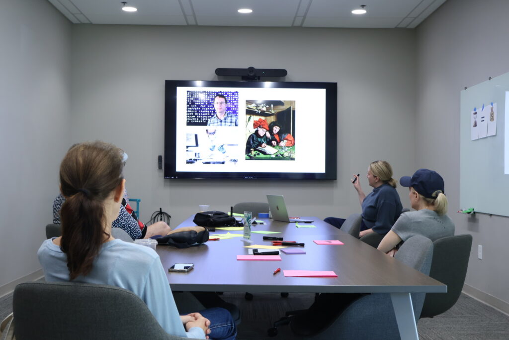 A group of people look at a television with images of inventors and code on it.