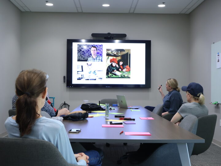 A group of people look at a television with images of inventors and code on it.