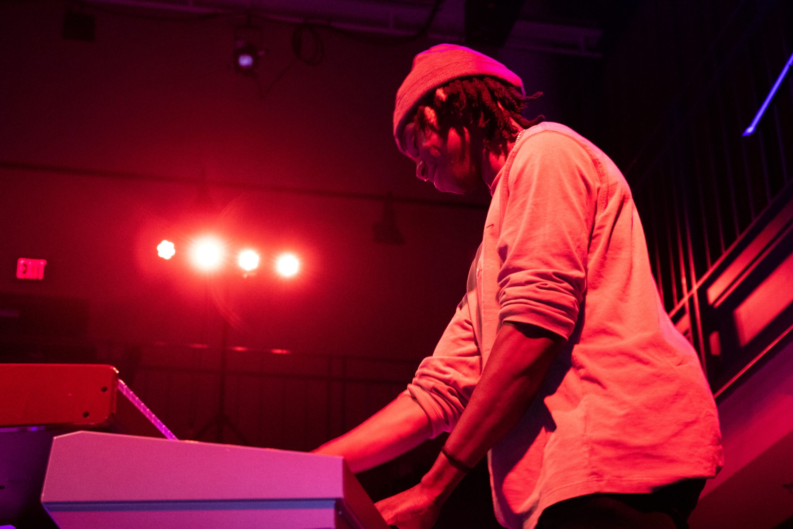 A musician playing keyboard under red stage lights at a Hurt Hub event