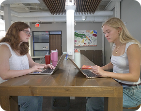 Two students working on laptops at a shared table