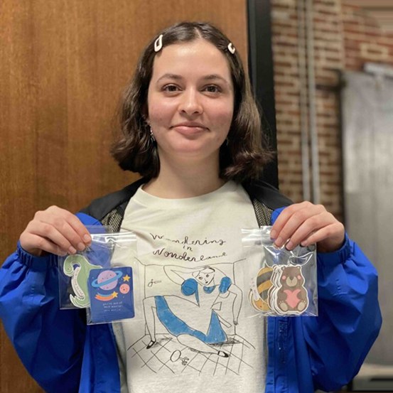 A student holding up two packs of her hand-drawn keychains