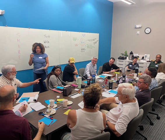 A facilitator leading a workshop around a large table at the Hurt Hub
